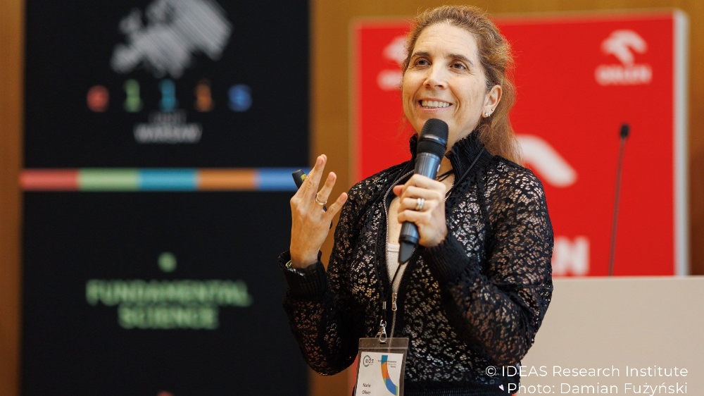 Nuria Oliver, ELLIS Board Member, speaking into a microphone at the ELLIS Doctoral Symposium 2025 in Warsaw