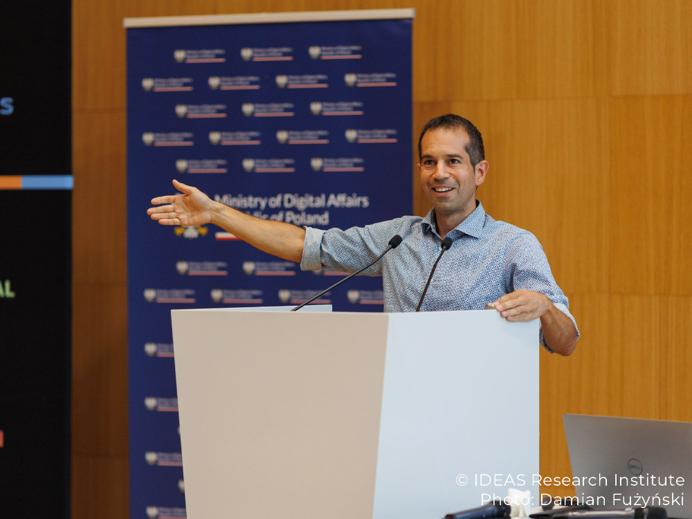 A man is standing in front of a podium gesturing to his right side