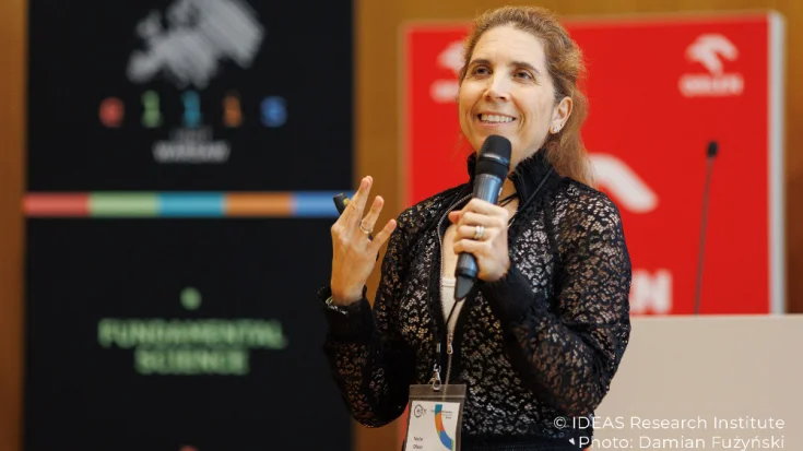 Nuria Oliver, ELLIS Board Member, speaking into a microphone at the ELLIS Doctoral Symposium 2025 in Warsaw