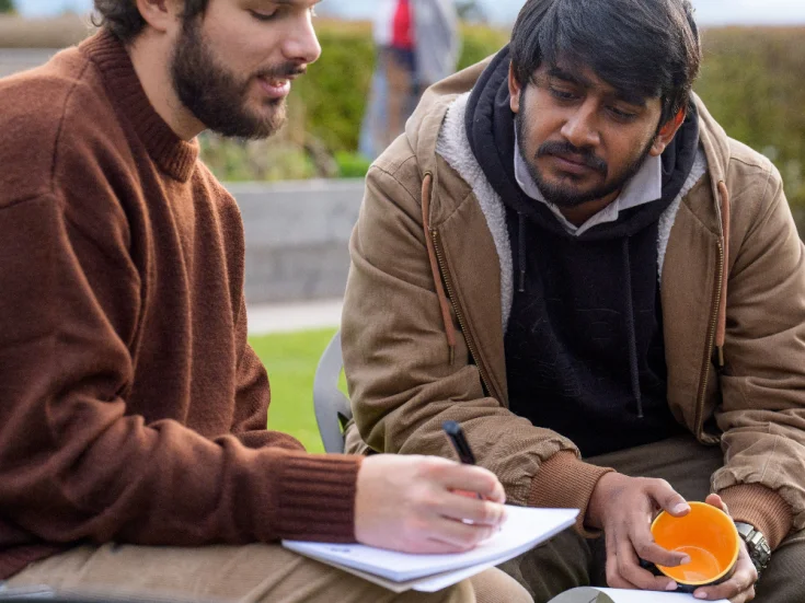 two men looking at a pad of paper, one is holding a pen and writing