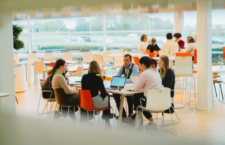 A group of women and a man sitting at a table talking and looking at an open laptop