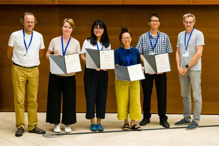 ELLIS PhD Award recipients in 2019 standing in between Bernhard Schoelkopf and Bernt Schiele