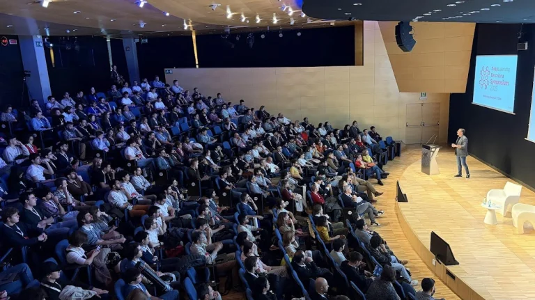 ELLIS Pre-NeurIPS Fest 2025: Unit Barcelona, a large auditorium filled with people and a man speaking on stage